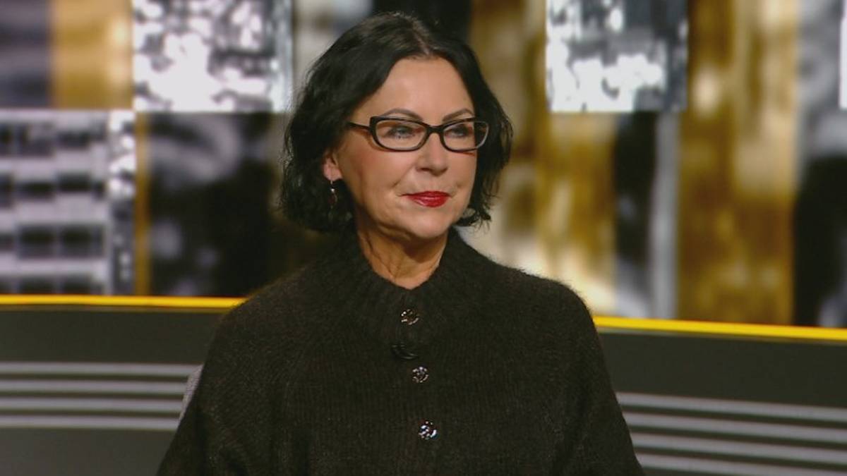 Portret kobiety w okularach, z ciemnymi włosami i czerwoną szminką na ustach, ubraną w ciemny sweter.