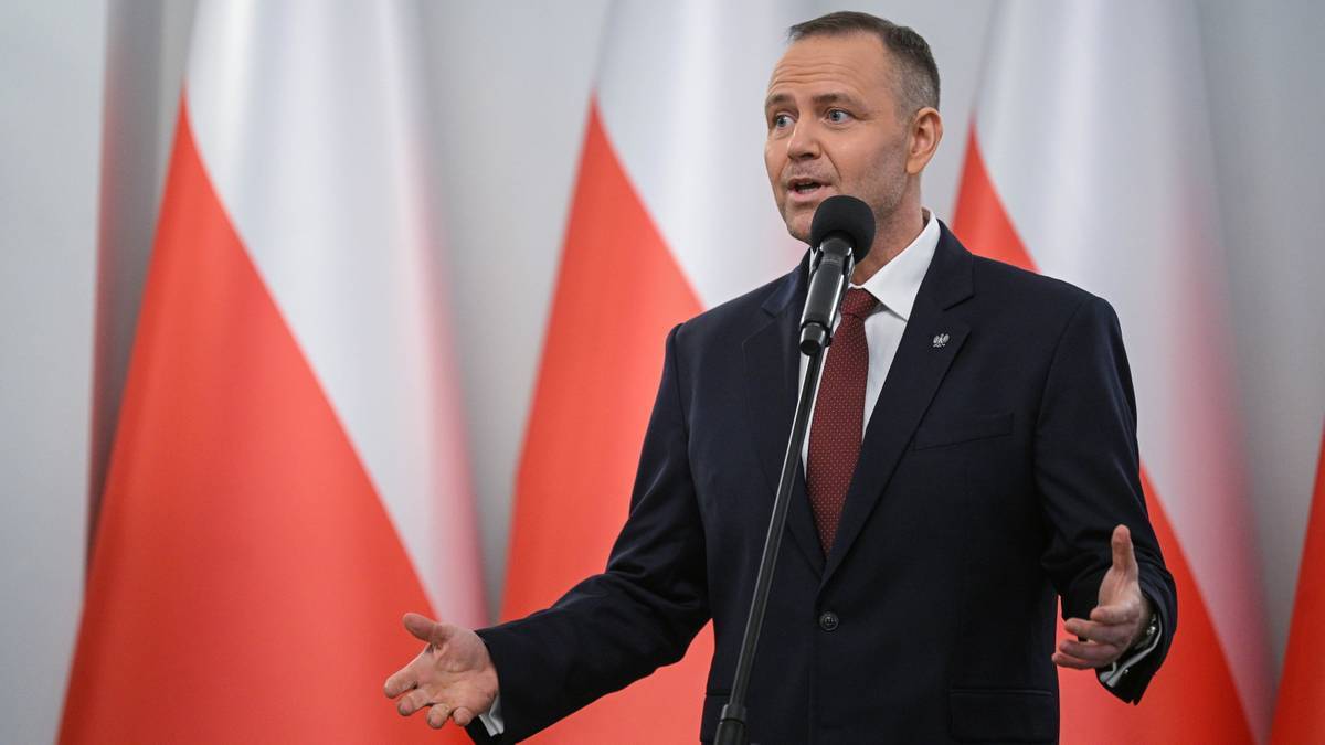 Prezydent RP Karol Nawrocki przemawia do mikrofonu na tle flag Polski.