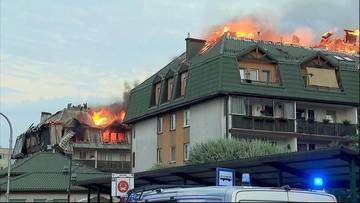 Widok na płonące poddasze budynku mieszkalnego w Ząbkach, z dymem unoszącym się nad dachem.