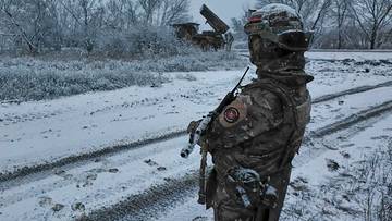 Żołnierz w zimowym kamuflażu stoi na zaśnieżonej drodze, trzymając broń.