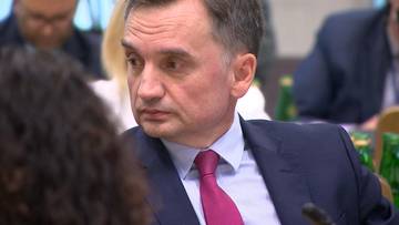 Mężczyzna w garniturze i r&oacute;żowym krawacie, siedzący przy stole.