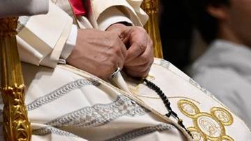 Zbliżenie na dłonie papieża Leona XIV trzymające r&oacute;żaniec, ubrane w białe szaty z ozdobnym haftem.