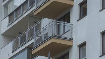 Fragment fasady bloku mieszkalnego z kilkoma balkonami, widoczne szklane balustrady i dwa ptaki na jednym z balkon&oacute;w.